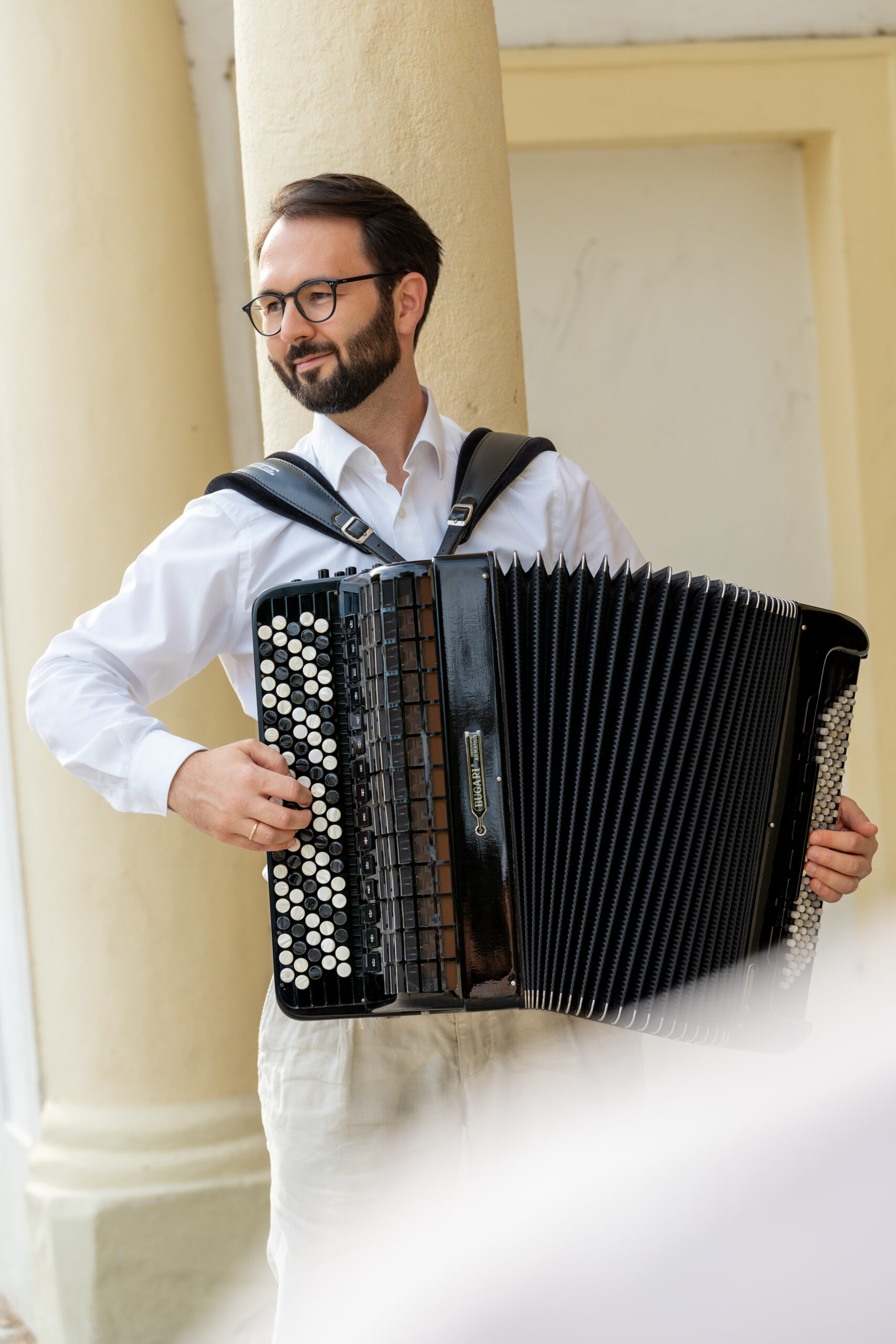 Nikola Djoric mit geöffnetem Akkordeon vor einer Steinfassade.