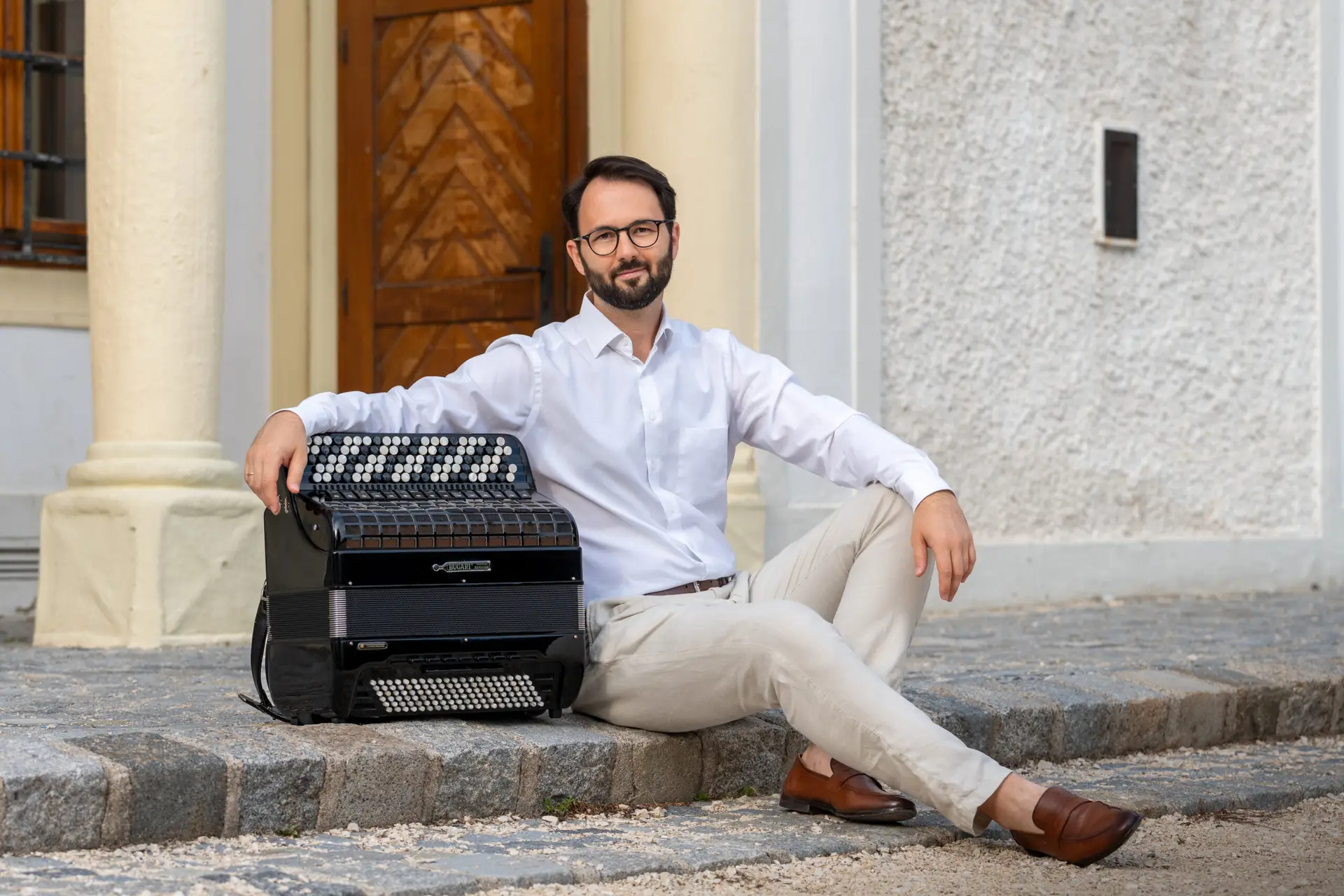 Nikola Djoric sitzt mit seinem Akkordeon auf Stufen.